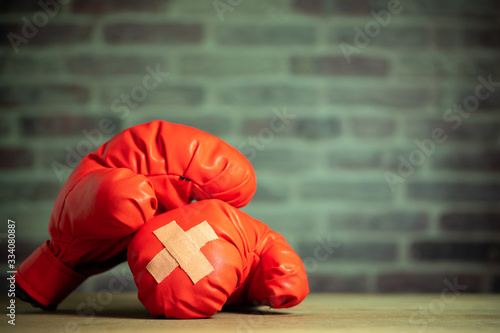 Red boxing gloves on wooden table and brick wall at the sport gym. Adhesive plaster across each other on boxing gloves. Idea of getting hurt or combat losing business rival. Fighting giving up boxing