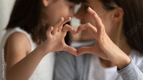 Close up of young mother and cute little daughter make heart sign with hands enjoy close tender moment together, caring mom and grateful small girl child show love and support in family relationships photo