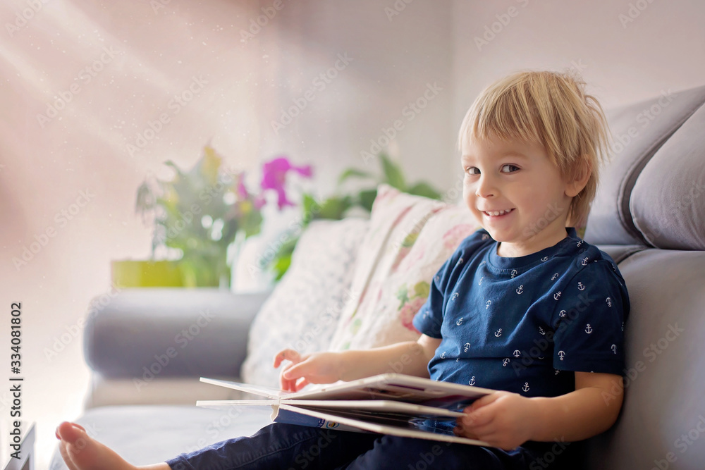Young woman, mother with three kids, reading a book at home, hugging and laughing Young woman, mother with three kids, reading a book at home, hugging and laughing