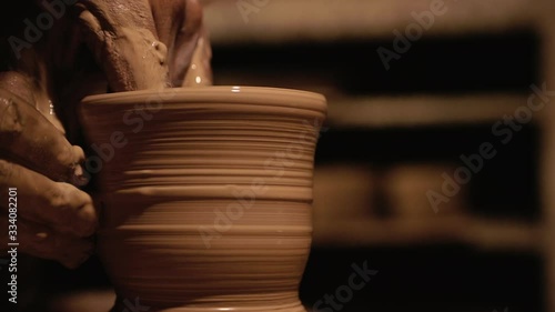 Young handsome sculptor shapes the clay product with pottery tools. Artisan potter prepares material for his pottery. Strong man hands working clay on potter's wheel. Work close-up.