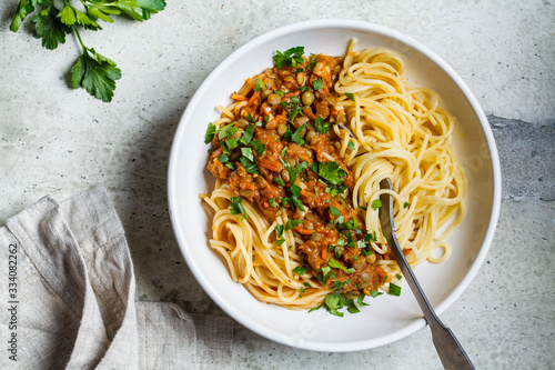 Vegetarian lentils bolognese pasta with parsley in white dish, top view. Healthy vegan food concept.