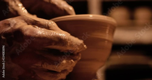 Young handsome sculptor shapes the clay product with pottery tools. Artisan potter prepares material for his pottery. Strong man hands working clay on potter's wheel. Work close-up.