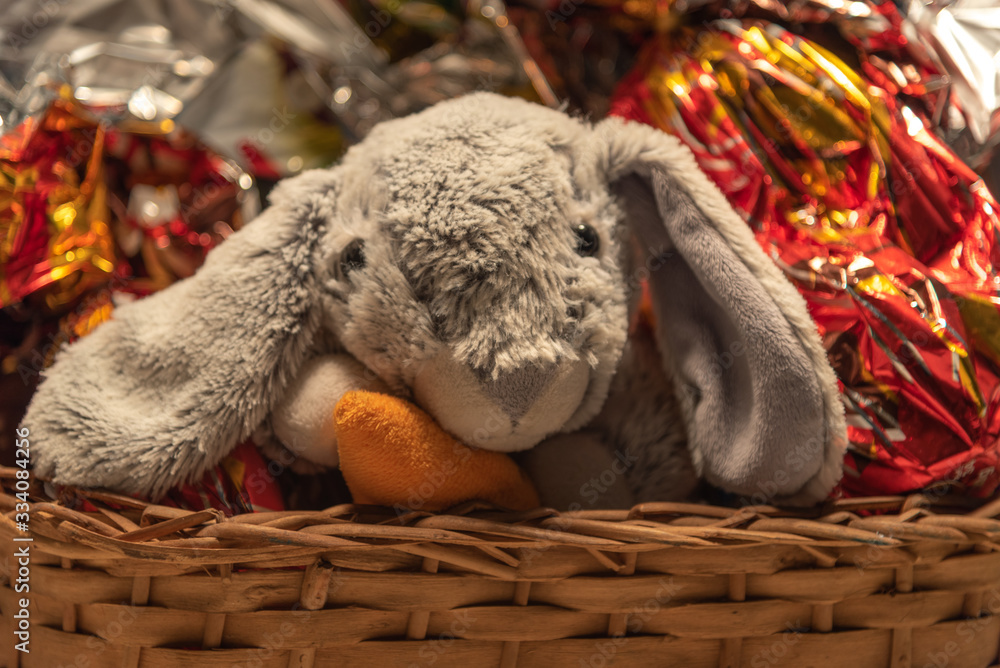 Obraz premium Plush rabbit in wicker basket with chocolate eggs for Easter party