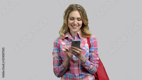 Attractive glamour girl with purse chatting with someone online. Smartphone messanging. Isolated on grey background. photo