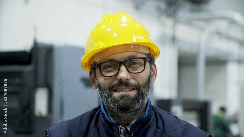 Closeup view of smiling professional engineer looking at camera. Cheerful mature engineer posing at factory. Manufacturing employee concept Closeup view of smiling professional engineer looking at camera. Cheerful mature engineer posing at factory. Manufacturing employee concept