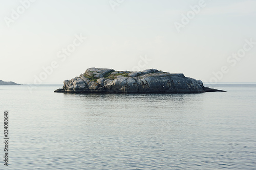Fototapeta Uninhabited small isle with smooth granite rocks and green moss, lichen in blue Arctic Ocean in clear day, horizon, arctic landscape