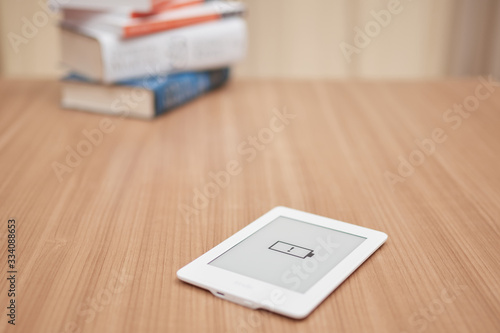 e-reader, kindle, with low battery symbol, in the background a stack of unfocused books