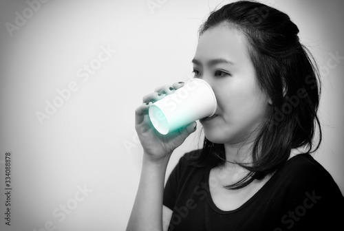Asian young woman drinking a fresh white paper cup of water or other beverage.bllack and white tone