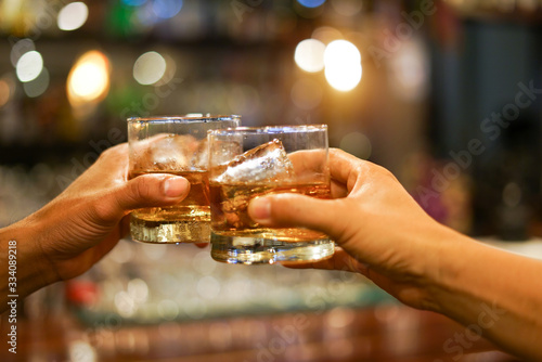 Fotografering Two men clinking glasses of whiskey drink alcohol beverage together at counter i