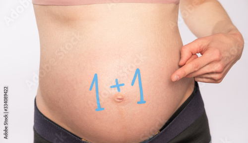 Belly of a pregnant woman with the inscription “1 + 1"