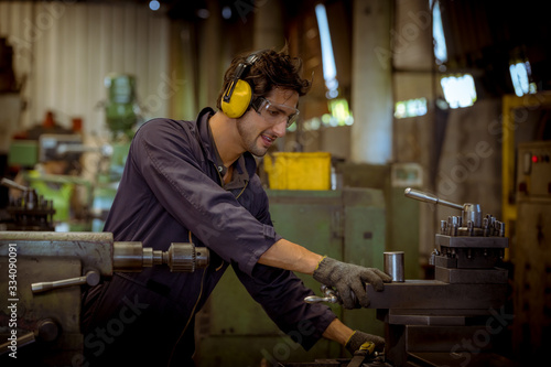 The Industry engineering wearing glass, ear phone and safety uniform used Vernier caliper to measure the object control operating machine working in industry factory. © APchanel