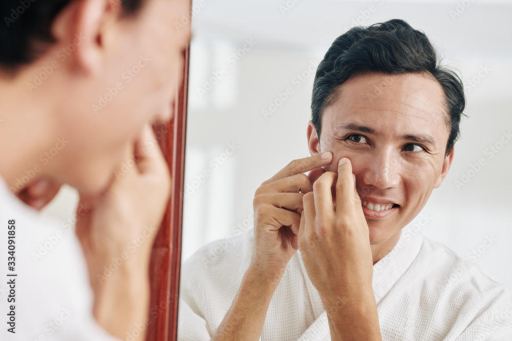 Smiling mixed-race man looking at mirror and squeezing pimples Smiling mixed-race man looking at mirror and squeezing pimples