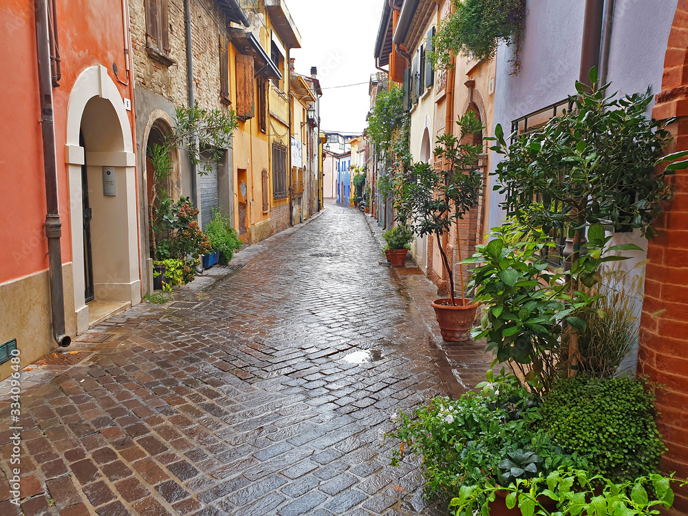 A colorful, narrow, deserted street in Rimini on a rainy, overcast day.