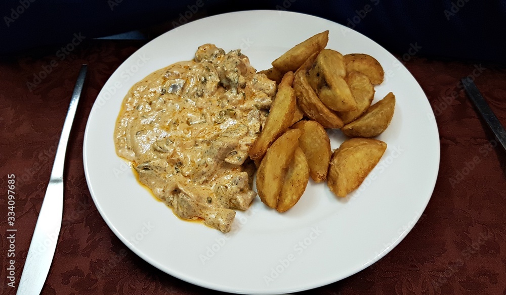 Sliced cooked meat with mushroom sauce and potatoes on a white plate Sliced cooked meat with mushroom sauce and potatoes on a white plate