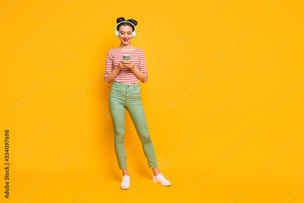 Fototapeta premium Full length photo of pretty lady use telephone turn on favorite melody modern technology earphones wear red white shirt green pants footwear isolated bright yellow color background