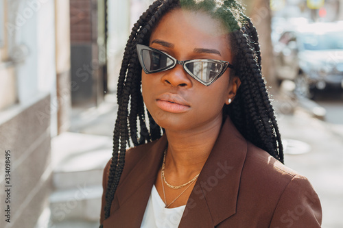 Close up portrait of a beautiful young african american woman with pigtails hairstyle in a brown business suit walks along spring streets