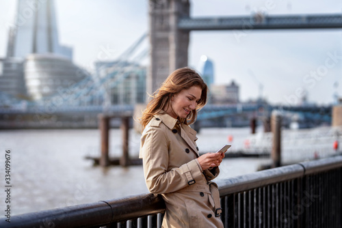 Photography Eine attraktive Frau im Trench Coat Mantel steht an der Themse vor der Skyline v