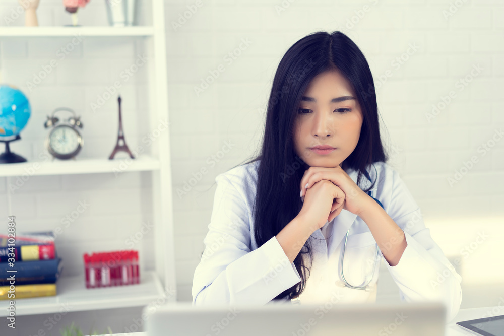 Asian female doctor is thinking about the result of an examination of her patients. Emotion with the young woman doctor being exhausted. Pensive nurse reading some information on the laptop screen Asian female doctor is thinking about the result of an examination of her patients. Emotion with the young woman doctor being exhausted. Pensive nurse reading some information on the laptop screen