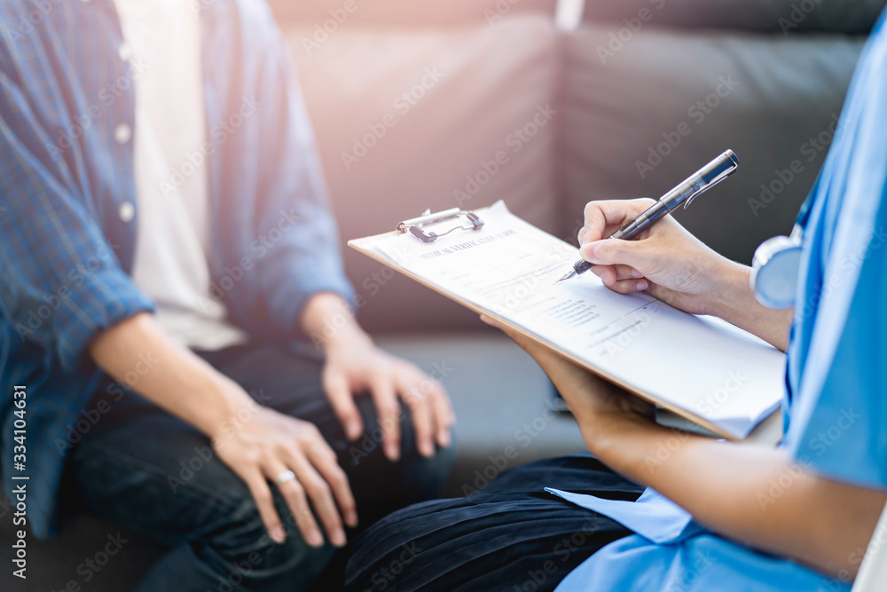 Close up female doctor writing and filling out forms on patient’s diagnosis information, with patient’s hands laid on the knee in stress and worry, with doctor holding clipboard pen in hospital office Close up female doctor writing and filling out forms on patient’s diagnosis information, with patient’s hands laid on the knee in stress and worry, with doctor holding clipboard pen in hospital office