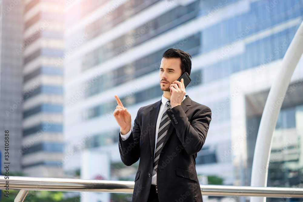 handsome caucasian businessman in a phone call talking and explaining information seriously while pointing a finger up, standing on a platform bridge with tall building and busy road in the background handsome caucasian businessman in a phone call talking and explaining information seriously while pointing a finger up, standing on a platform bridge with tall building and busy road in the background