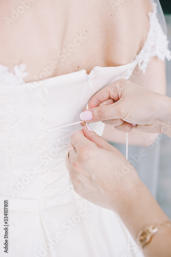 mom helps the bride to put on a dress