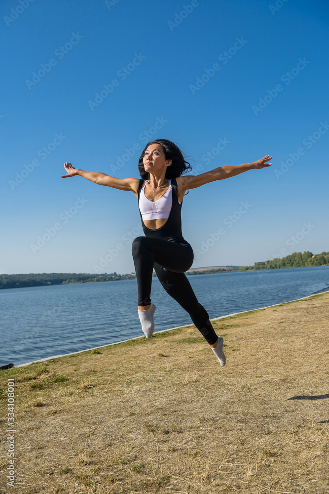 Smiling young female gymnast is jumping in split outdoors near the lake. Healthy lifestyle Smiling young female gymnast is jumping in split outdoors near the lake. Healthy lifestyle