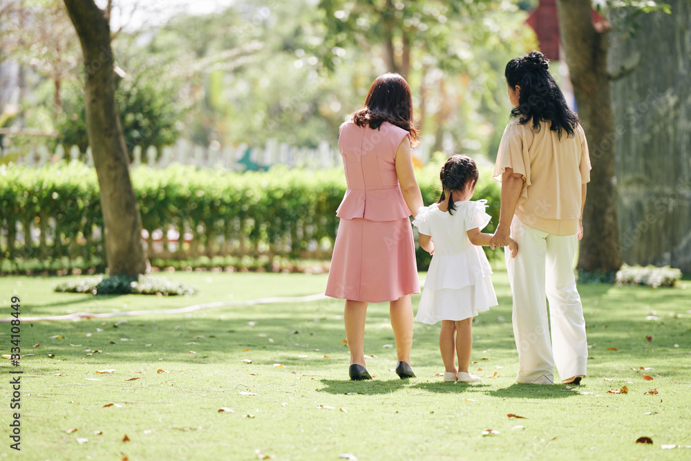 Fototapeta premium Senior woman enjoying spending time with her adult daughter and little granddaughter in park, view from the back