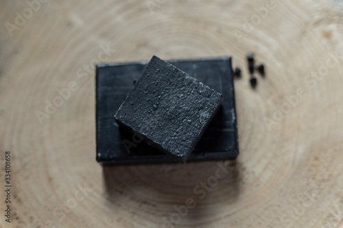 Fototapeta Naklejka Na Ścianę i Meble -  charcoal coal carbon black soap bar on a raw wood background lava stone spa skin care hygiene concept 