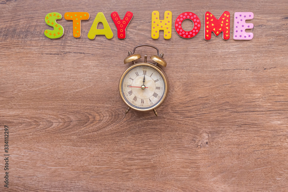 Inscription STAY HOME of wooden letters and alarm clock on wood background with copy space Inscription STAY HOME of wooden letters and alarm clock on wood background with copy space