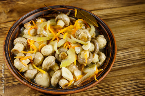 Delicious marinated mushrooms with carrot, onion and spices in ceramic bowl on wooden table