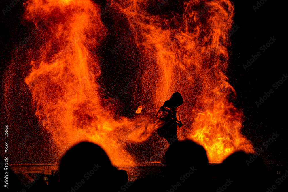 Silhouette of a firefighter fighting to contain a raging fire as a crowd looks on