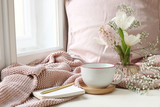 Cozy Easter, spring still life scene. Cup of coffee, notebook, golden pen, pink knitted plaid near window. Vintage feminine styled photo. Floral composition with tulips, hyacinth and Gypsophila