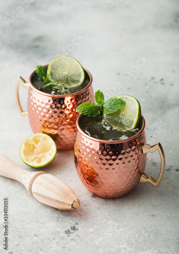 Moscow mule cocktail in a copper mug with lime and mint and wooden squeezer on light background