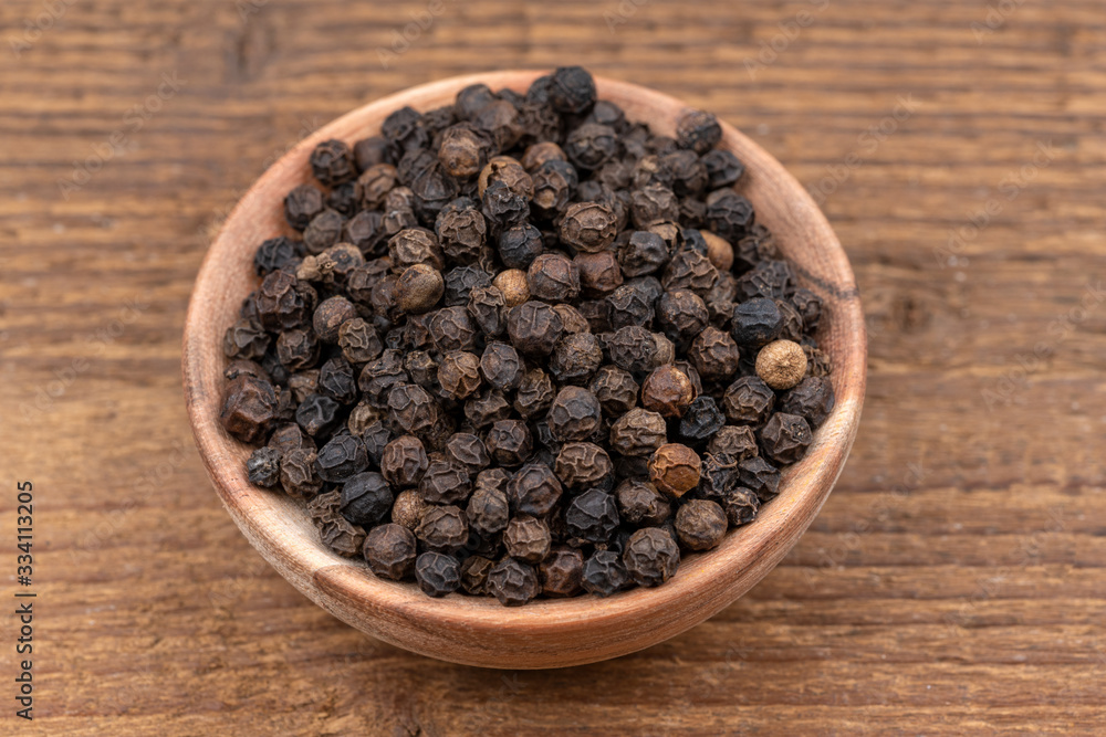 Whole black peppercorns in a small wooden bowl on a rustic wooden background Whole black peppercorns in a small wooden bowl on a rustic wooden background