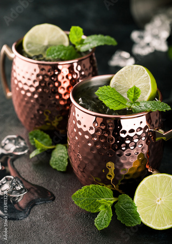 Moscow mule cocktail in a copper mug with lime and mint and wooden squeezer on dark kitchen table background with ice cubes