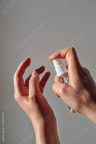 Woman hand holding and spray a sanitizer on a grey background with shadows from hand