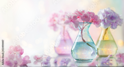 Bouquets of beautiful hydrangea in colorful glass vases over bokeh background...