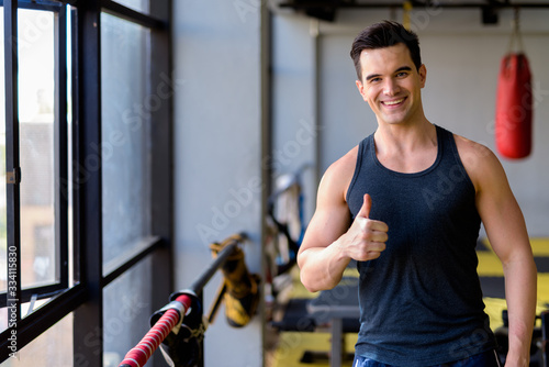 Happy young handsome man giving thumbs up at the gym