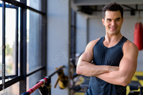 Happy young handsome man thinking with arms crossed at the gym