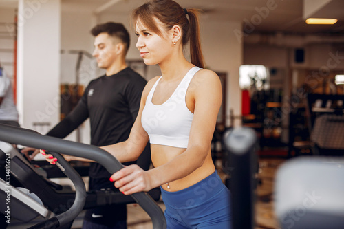 Couple in the gym. A woman performs exercises. Man in a black t-shirt © prostooleh