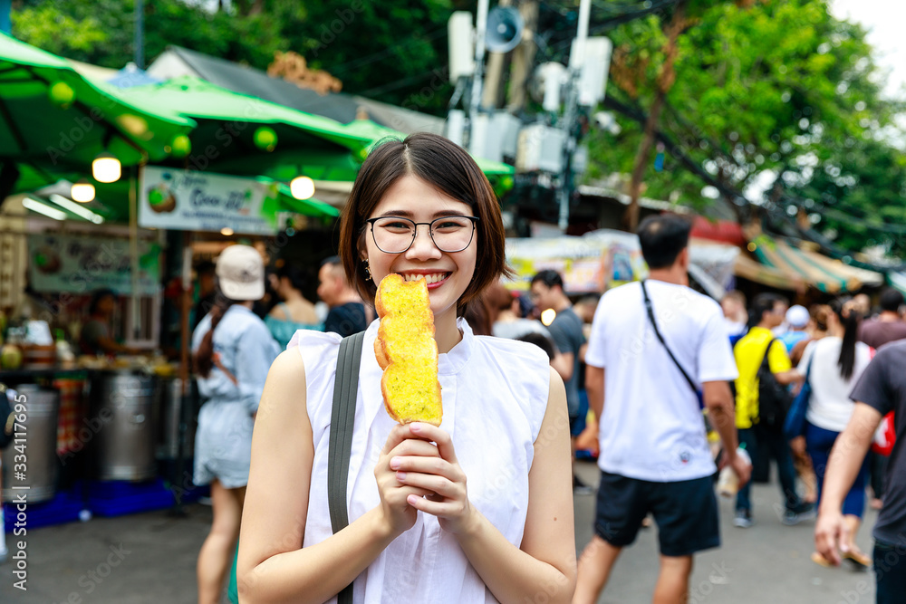 Asian young short hair beautiful woman wearing glasses enjoy eating butter toast at street market, street food Thailand