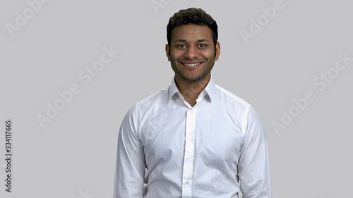 Portrait of happy young brown-skinned man wearing white formal shirt. Cheerful hindy guy smiling with teeth. Grey isolated background. photo