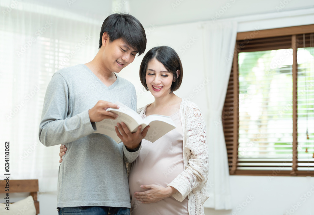 Young happy asian man and pretty pregnant woman reading book in home.Future father and pregnancy mother smile, laugh and enjoy together,family concept Young happy asian man and pretty pregnant woman reading book in home.Future father and pregnancy mother smile, laugh and enjoy together,family concept