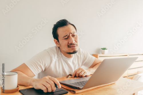 Serious Asian man is working with laptop in his apartment bedroom in concept of Work From Home and Work at Home.