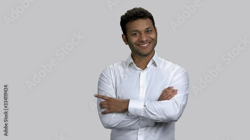 Happy cheerful hindu man with folded arms pointing left with his finger. Young brown-skinned guy. Grey isolated background.