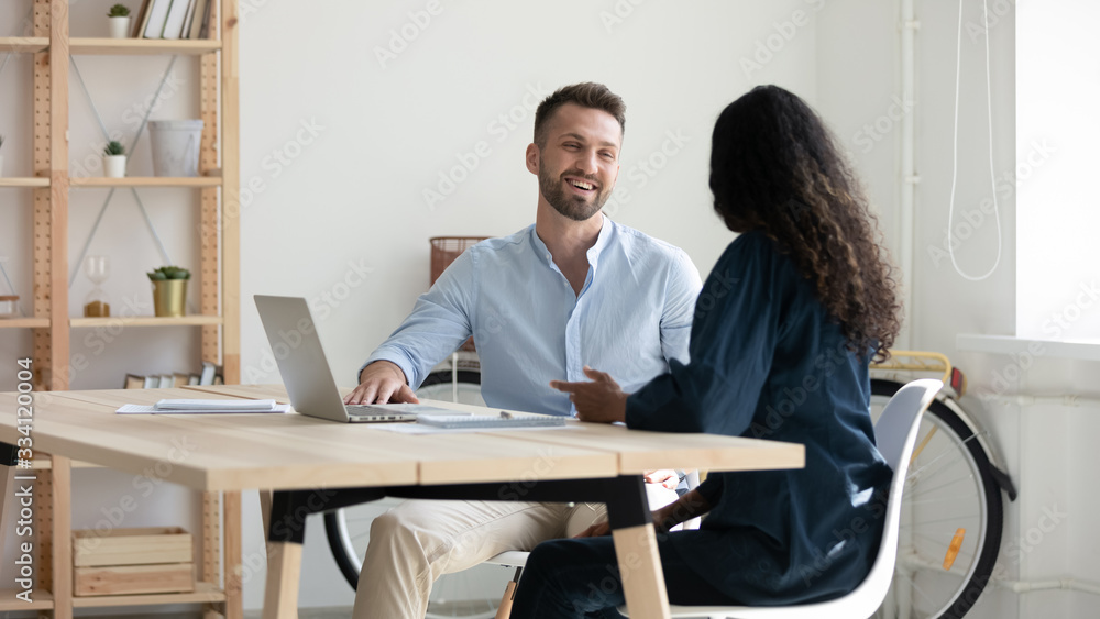 Smiling diverse businesspeople sit at desk brainstorm discuss business ideas together at casual briefing, happy colleagues talk laugh cooperate working on laptop at meeting in office, teamwork concept Smiling diverse businesspeople sit at desk brainstorm discuss business ideas together at casual briefing, happy colleagues talk laugh cooperate working on laptop at meeting in office, teamwork concept