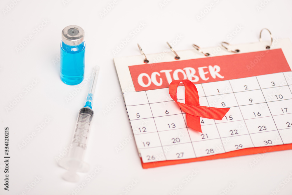 Selective focus of calendar with october month, aids awareness red ribbon with syringe and vaccine on white surface
