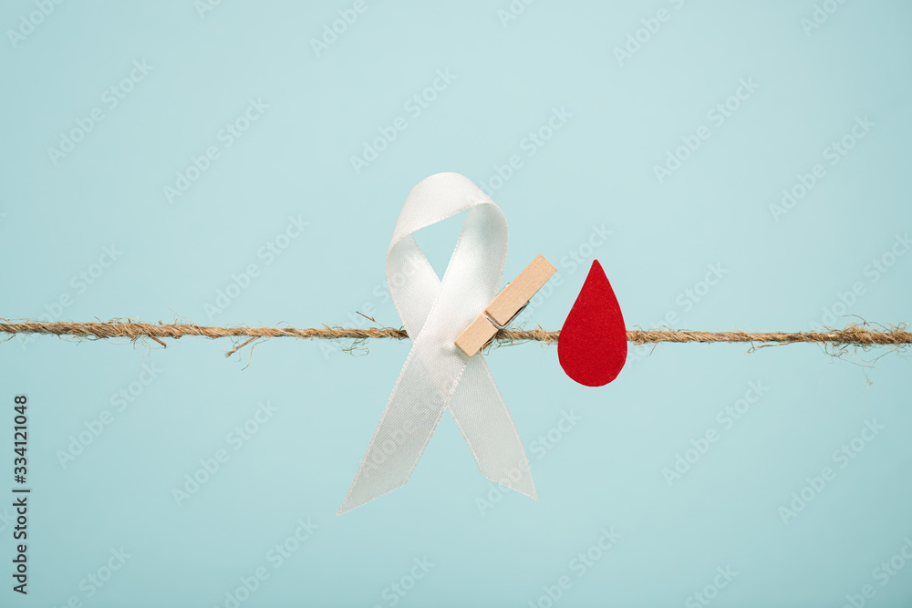White ribbon with pin and paper in blood drop shape on rope isolated on blue, hemophilia concept White ribbon with pin and paper in blood drop shape on rope isolated on blue, hemophilia concept