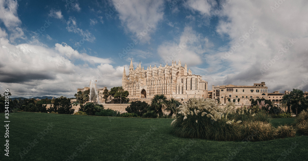 panorama of cathedral of palma de mallorca with green grass in foreground and dramatic cloudy sky