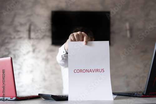 Człowiek w biurze z kartką w dłoni z napisem coronavirus